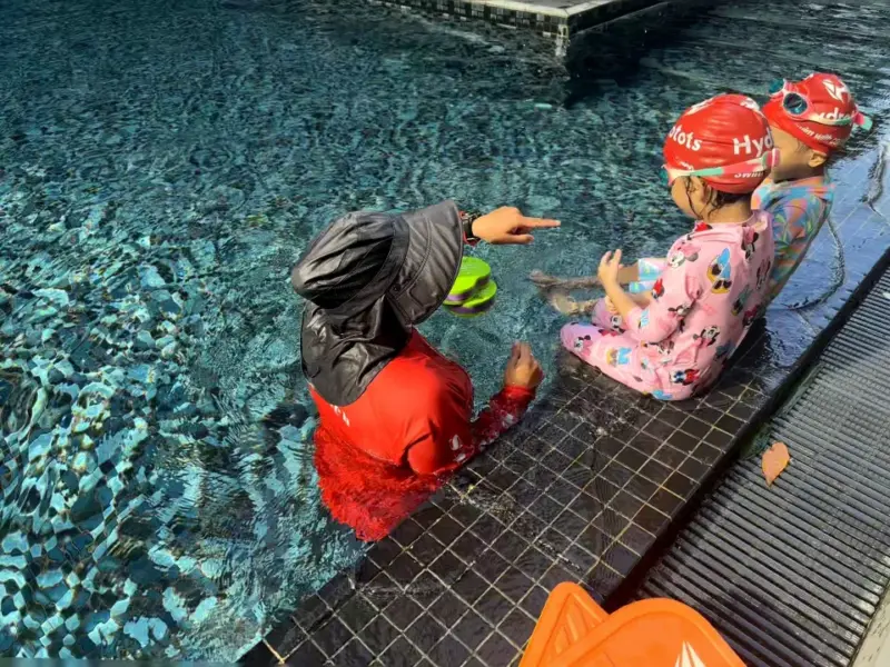 A coach teaching two young children at a condo pool