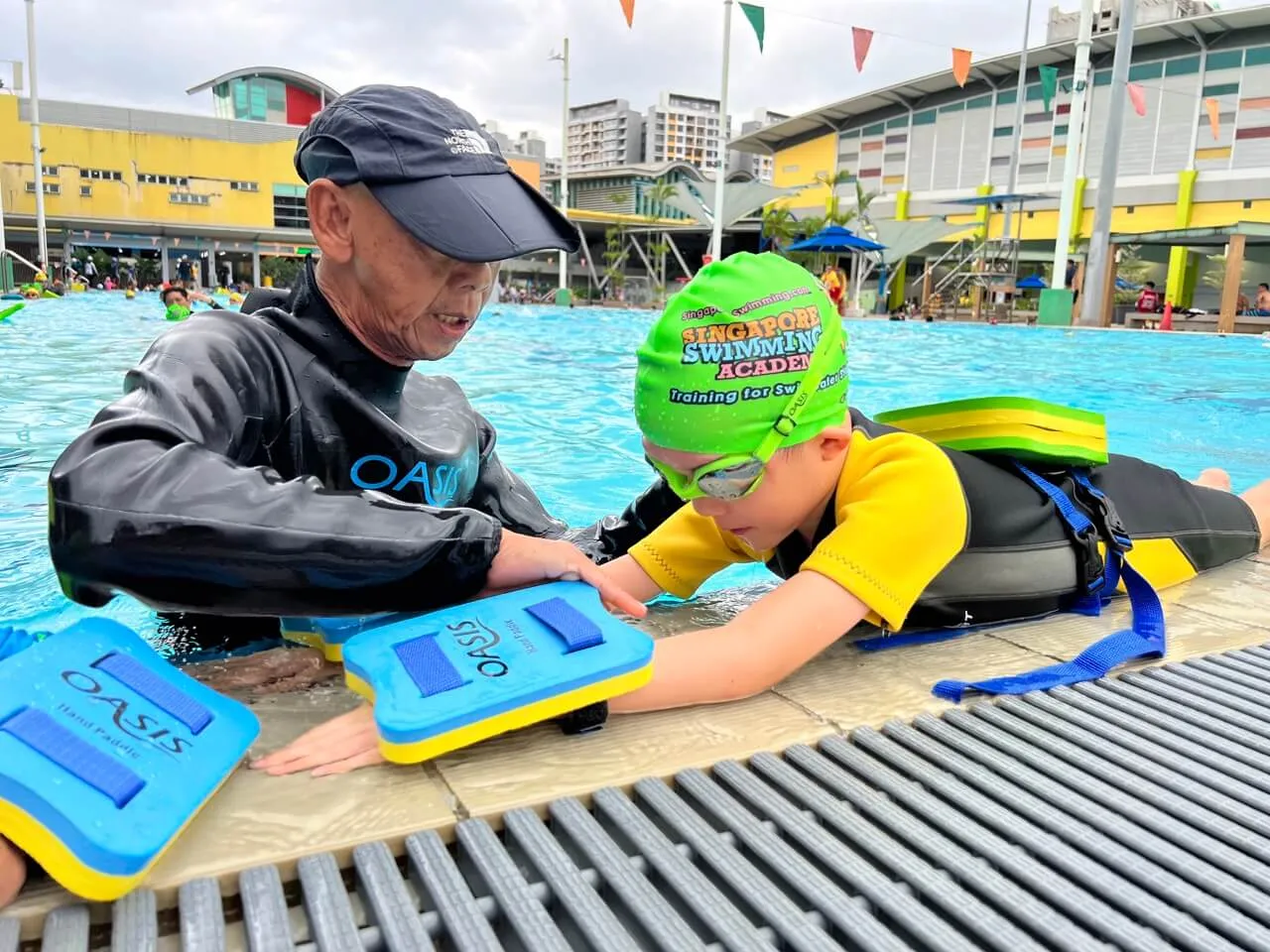 A coach teaching a boy to kick with floats at a public pool